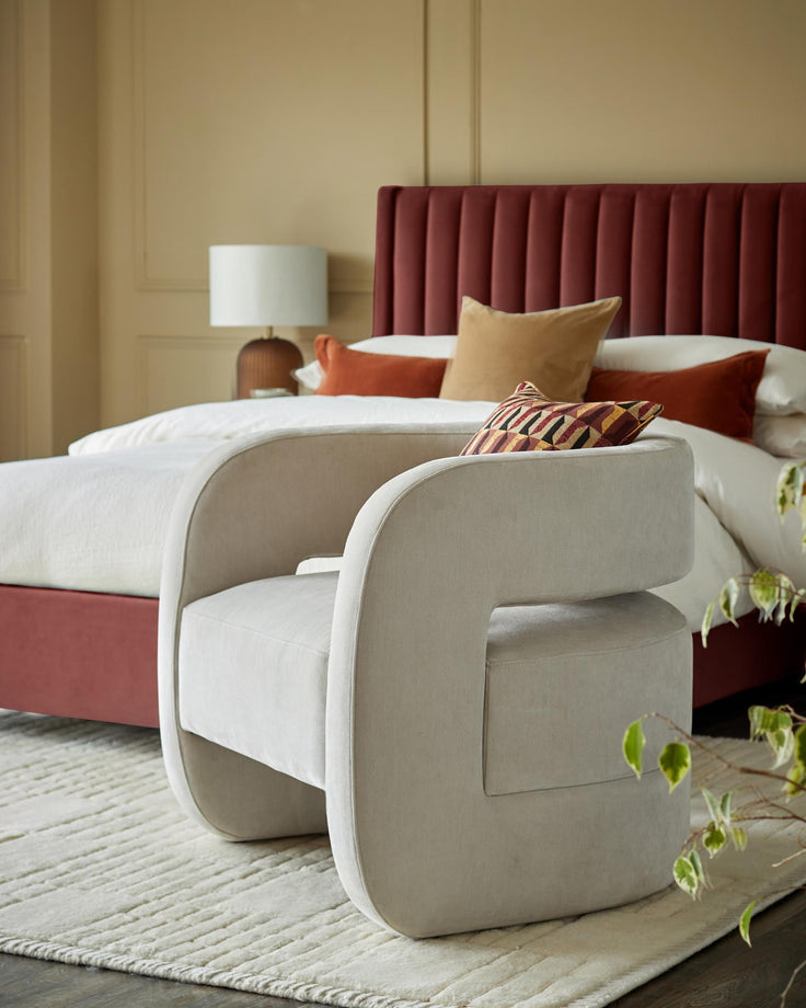 A stylish bedroom setting with a plush armchair in the foreground and a luxe bed with a padded headboard in the background.