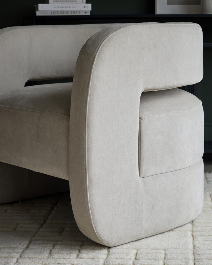 A modern, off-white chair with a unique curved design, sitting on a patterned cream rug.