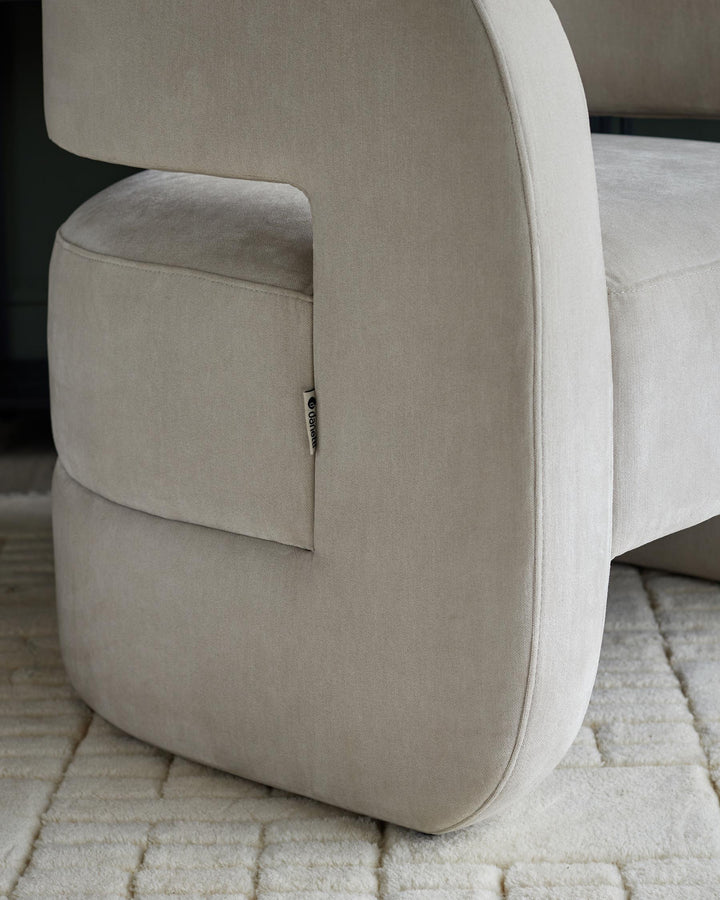 Close up of a stylish, curved light beige armchair with a patterned rug underneath.