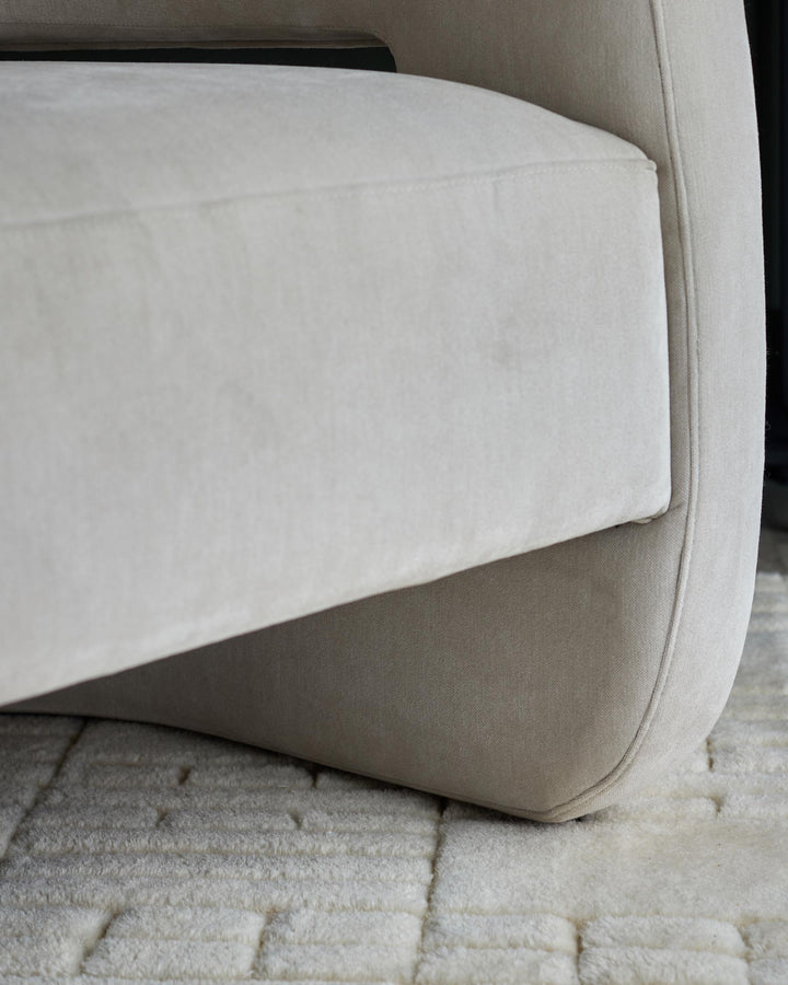 Close-up of a cream upholstered armchair, showing the arm and base with a textured rug underneath.