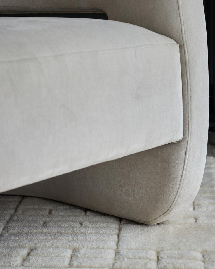 Close-up of a cream upholstered armchair, showing the arm and base with a textured rug underneath.