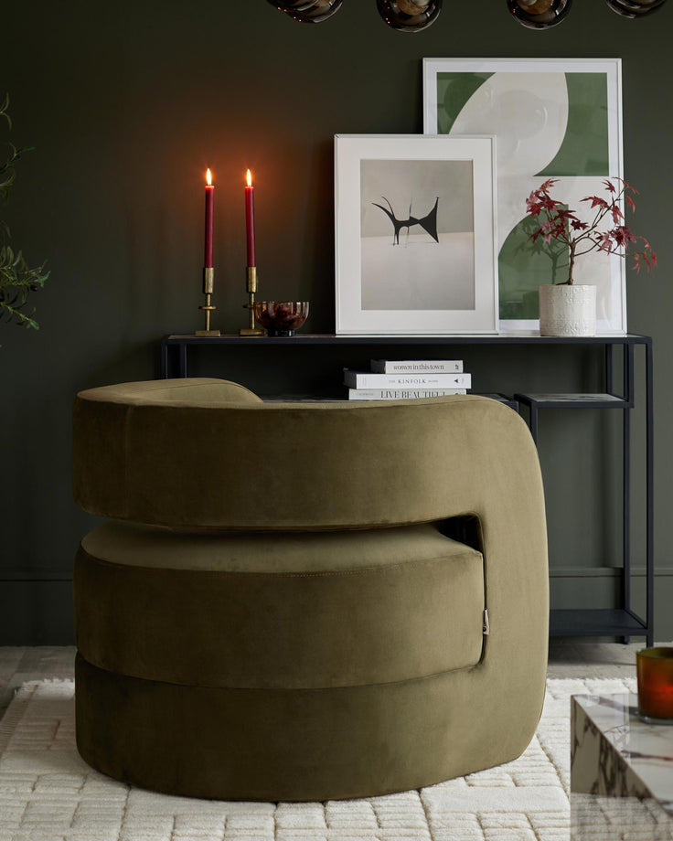 A stylish olive green velvet swivel chair sits in front of a dark metal console table with artwork and decorative items.