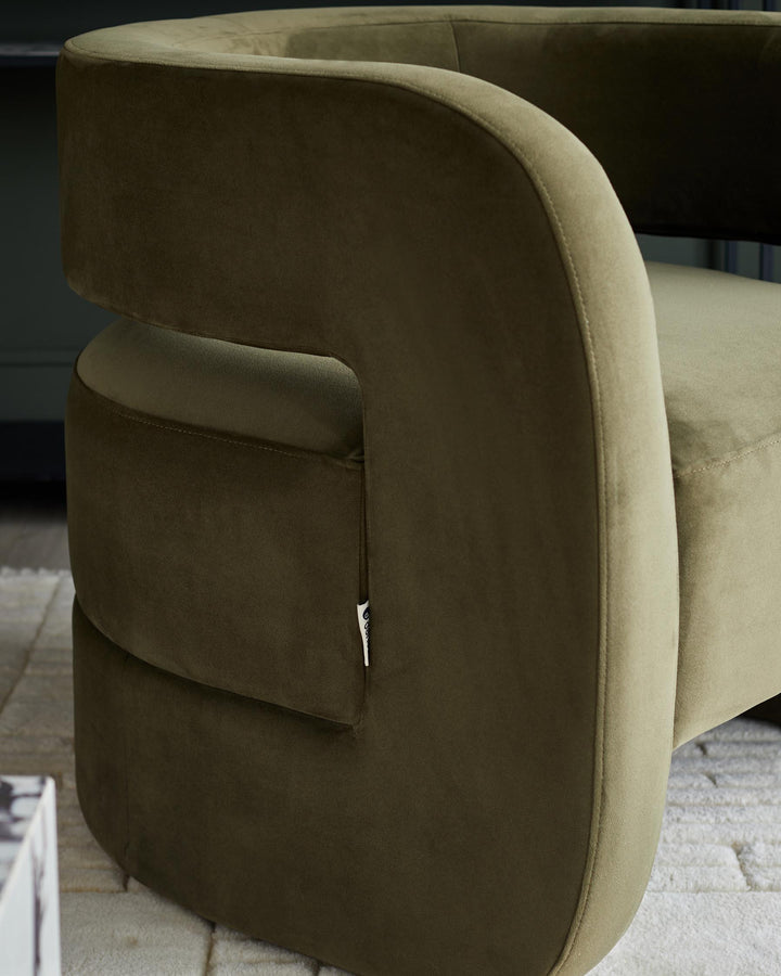 Close-up of an olive green velvet armchair, showing the curved armrest and soft texture.