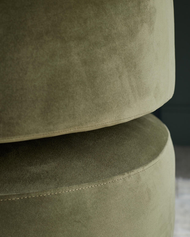 Close up of two round, olive green, velvet ottomans stacked on top of each other.