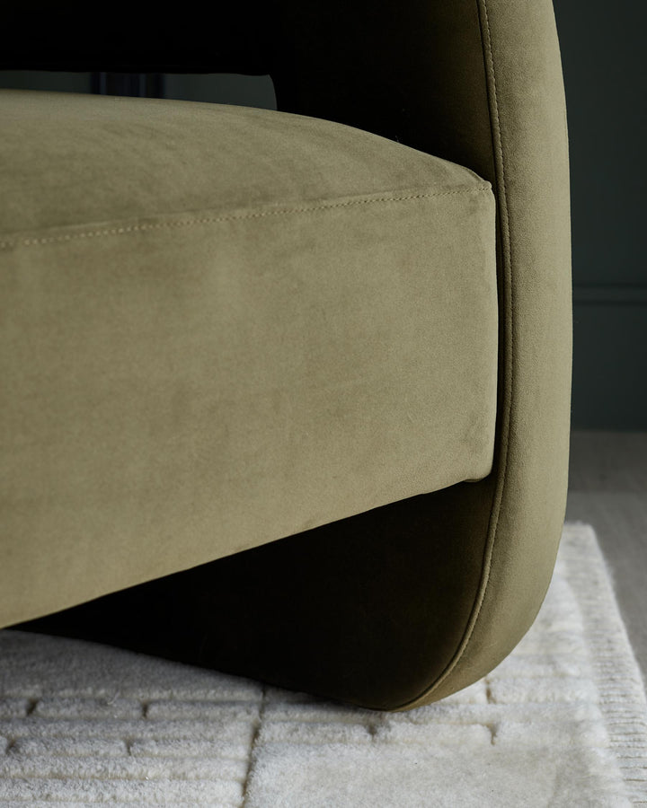 Close-up of an olive green upholstered chair, showcasing its curved arm and soft, textured fabric on a cream coloured rug.