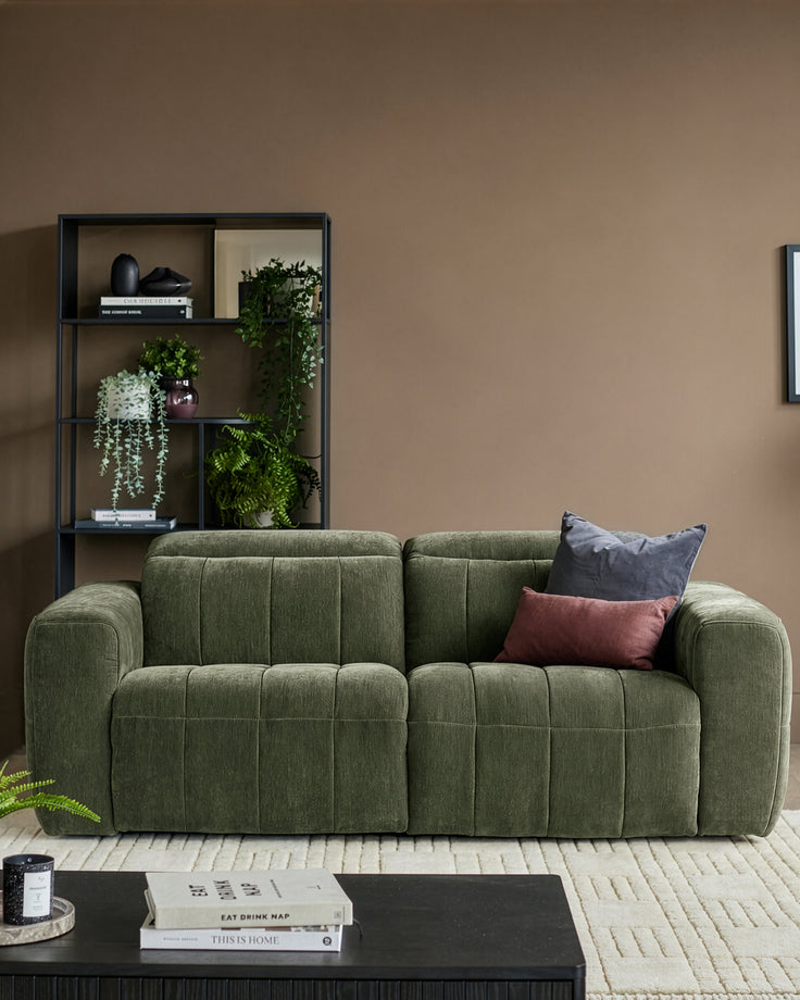 Skye 2-seater sofa in dark green fabric with quilted seat cushions and curved arms, styled in a modern living room.