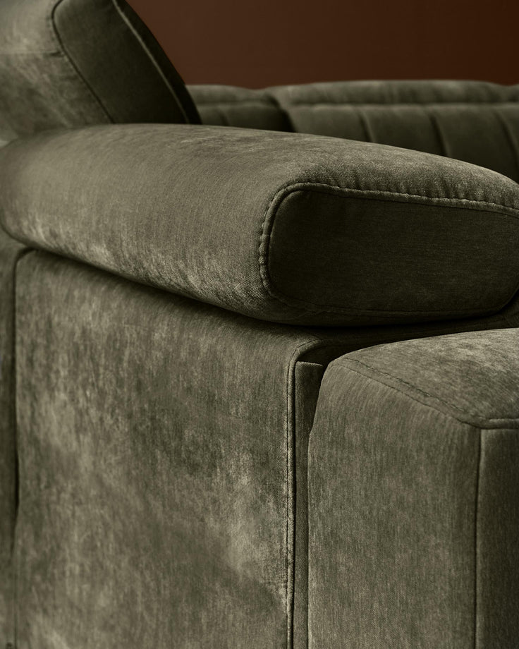 Dark green fabric corner sofa with rolled armrest and stitched seams, close-up detail view.