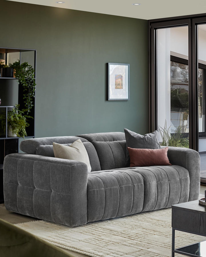 Stylish grey sofa with cushions in a modern living room setting, next to a side table and floor-to-ceiling windows.