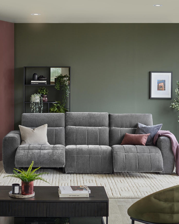 A grey three-seater sofa with reclining features, styled with cushions and throws, on a cream patterned rug.