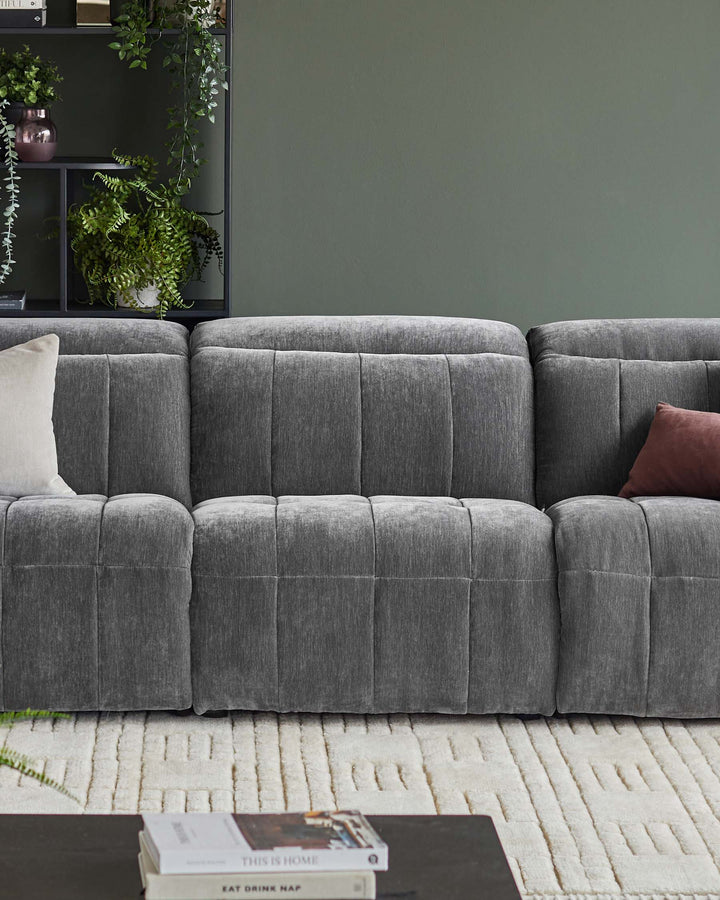 A plush, grey modular sofa with a geometric rug and a dark bookshelf with lush green plants.