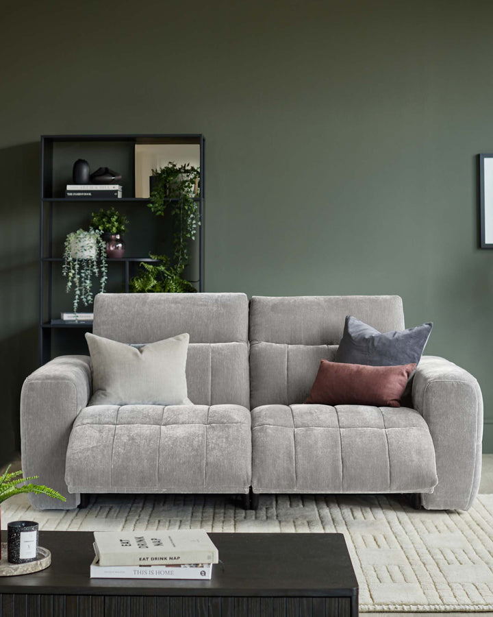 A modern grey sofa with scatter cushions, set against a dark green wall with black shelving and a patterned cream rug.