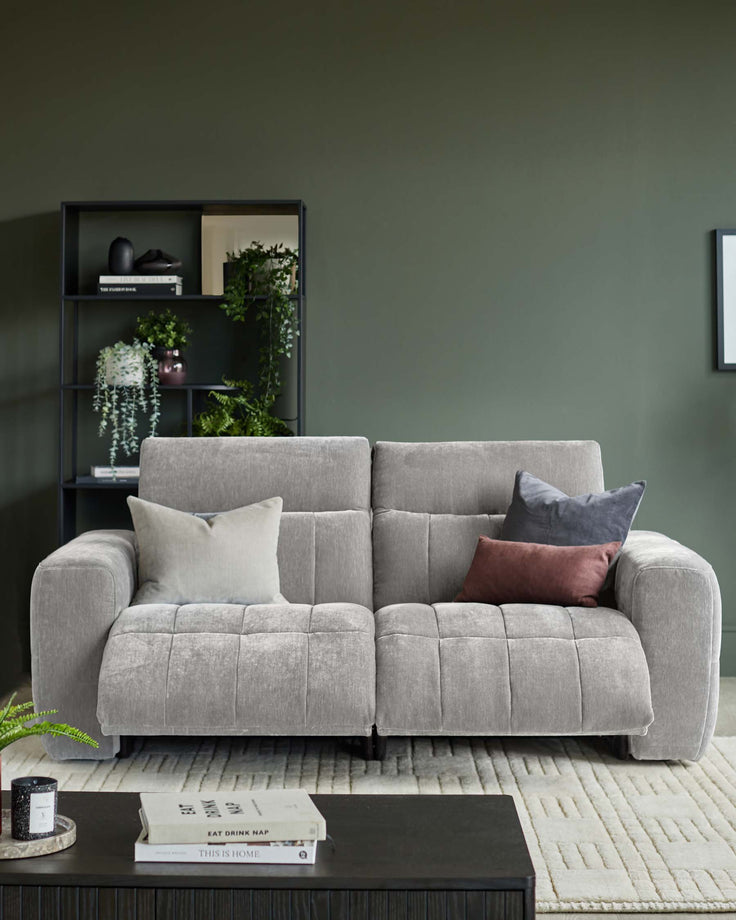 A modern grey sofa with scatter cushions, set against a dark green wall with black shelving and a patterned cream rug.