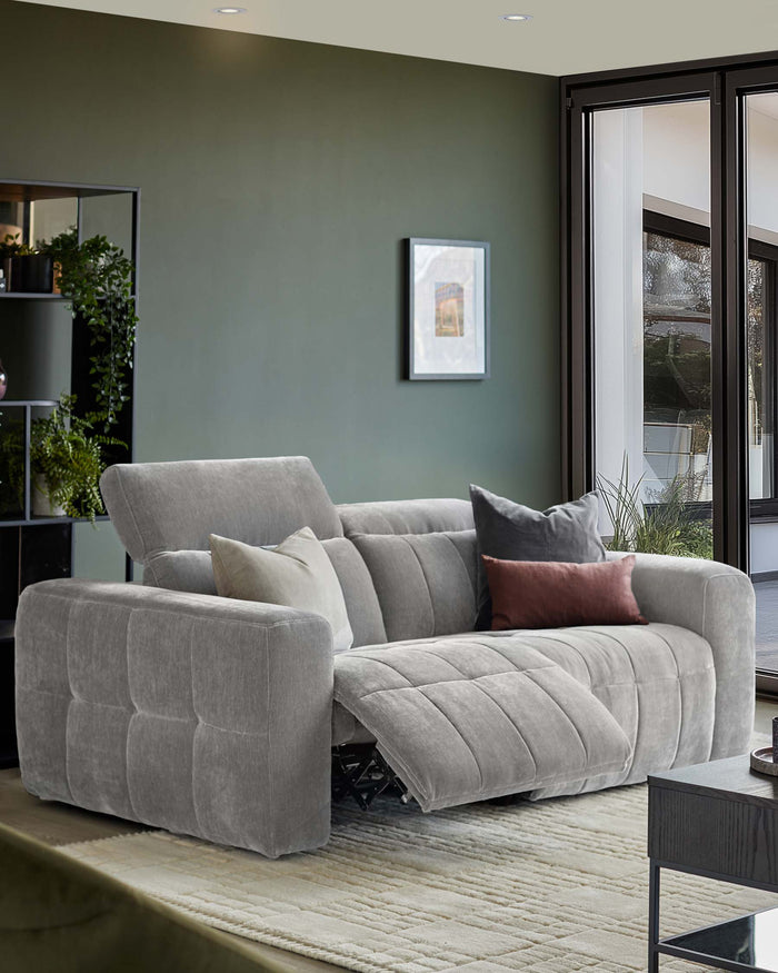 A stylish, grey, modular sofa with scatter cushions and a reclining footrest, situated in a modern living room.