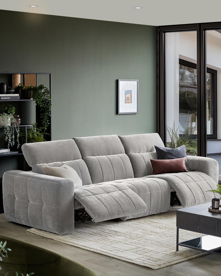 A comfy grey three-seater sofa with recliner seats, styled with cushions, sits on a neutral rug in a modern living room.