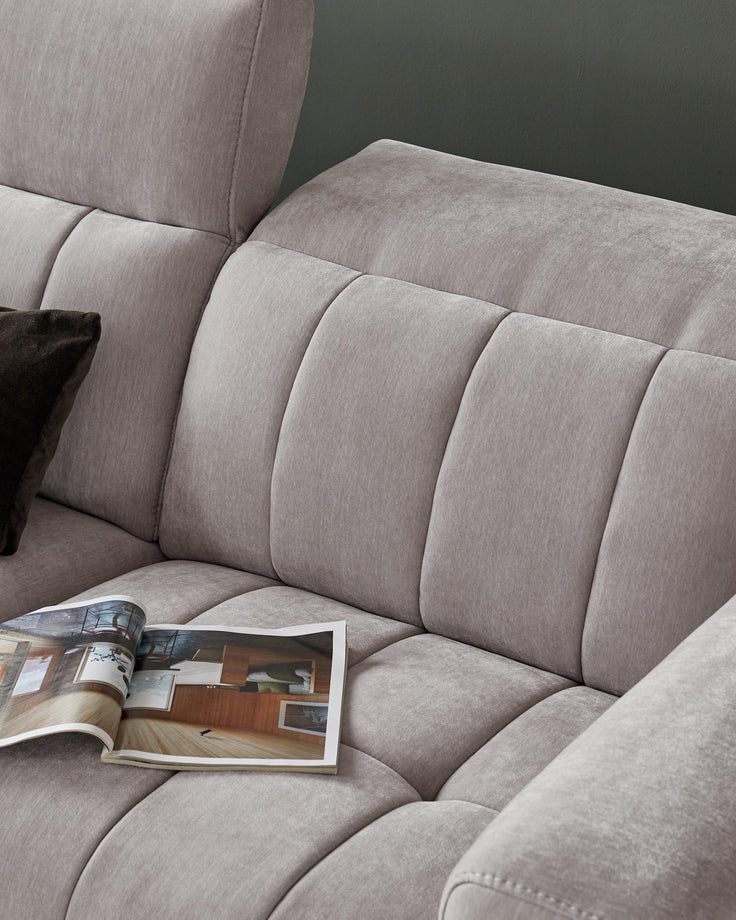 Close-up of a grey modular sofa with an open magazine on the seat, and a dark cushion. Comfortable seating.