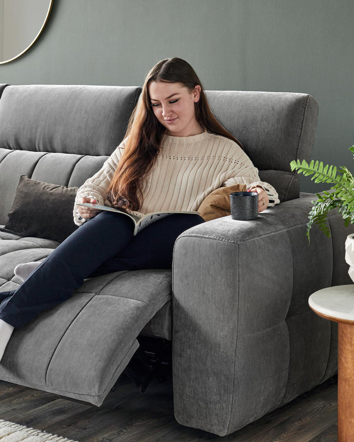 Modern gray sectional sofa with plush cushions, complemented by a wooden side table and a green plant for a cozy ambiance.