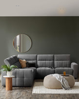 A plush gray sectional sofa with textured detailing, a round beige pouf, and a wooden side table adorned with greenery.