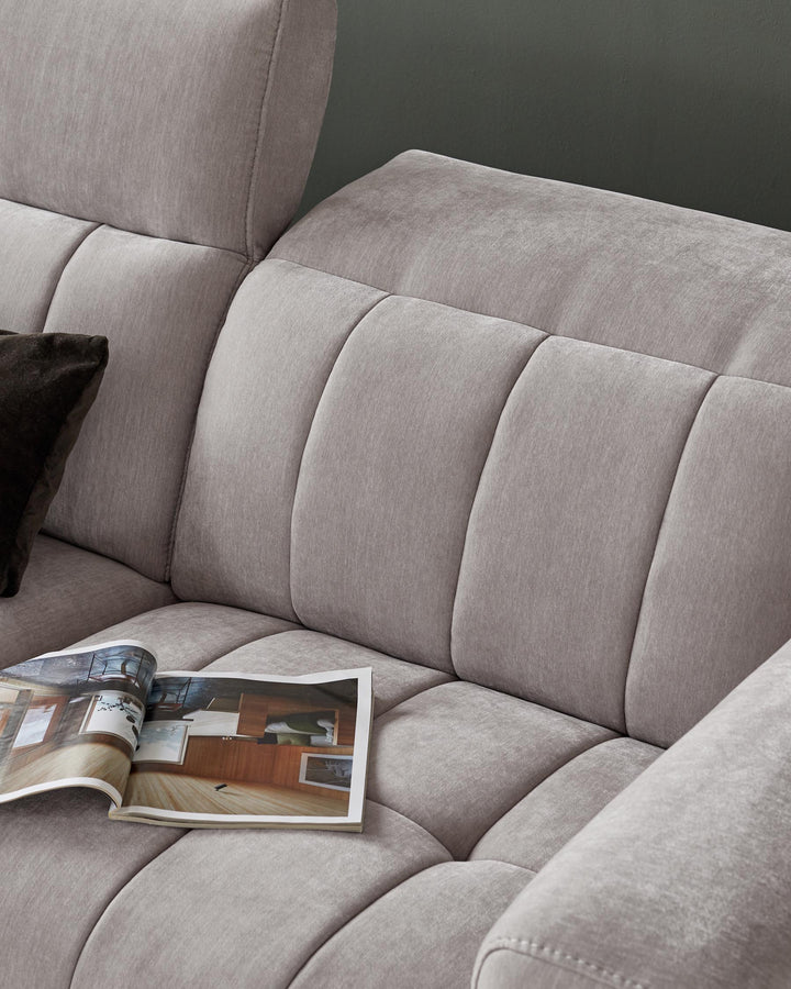 A modern, plush gray sofa with tufted cushioning, featuring a decorative pillow and an open magazine on the seat.