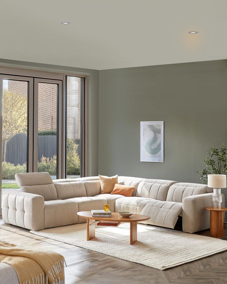 A spacious, cream-colored sectional sofa with plush cushions, a wooden coffee table, and a side table with a lamp.