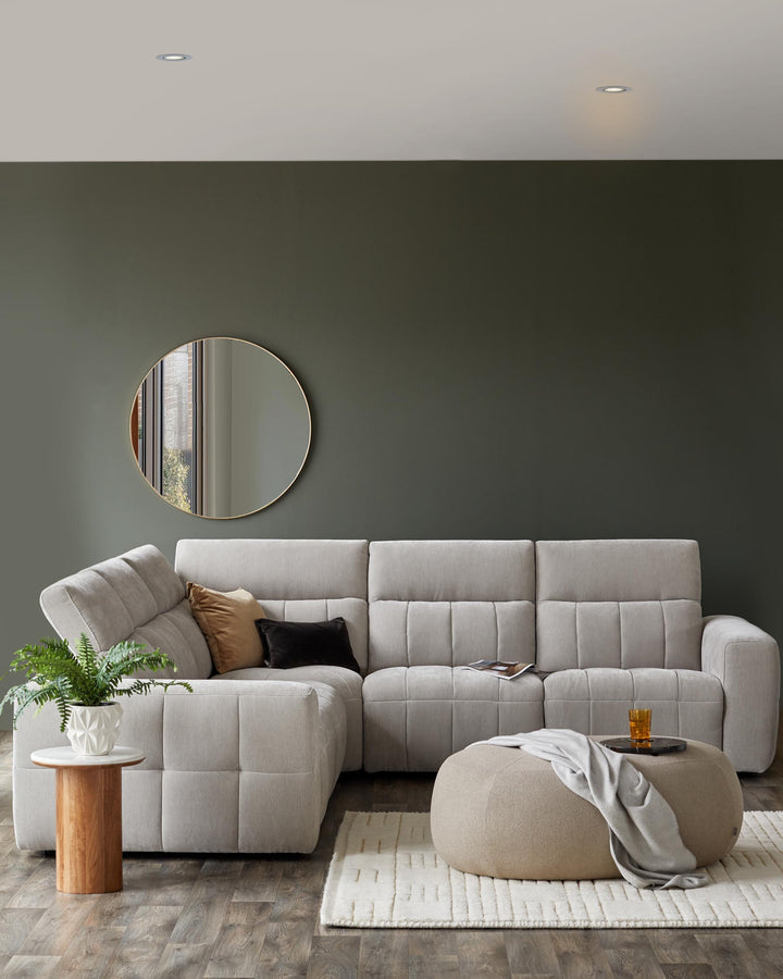 A light gray sectional sofa with textured cushions, a round mirror, an accent table, a soft ottoman, and a cozy rug.