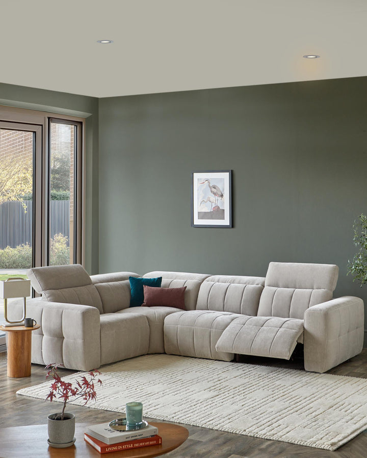 Modern L-shaped beige sectional sofa with tufted detailing, accented by colorful pillows, accompanied by a round side table and rug.