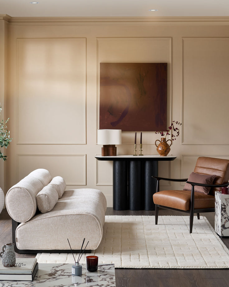 Sofia 2-seater sofa in natural fabric with curved design and cylindrical bolster pillows, displayed in a modern living room setting.