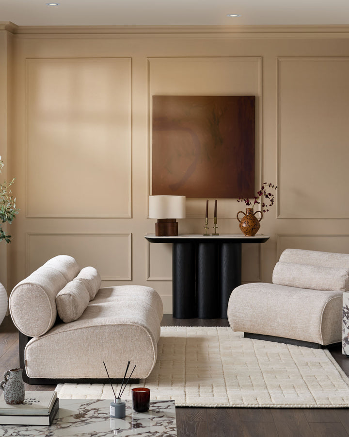 Sofia 3-seater sofa in natural fabric with curved arms and cylindrical bolster pillows, displayed in a contemporary living room setting.