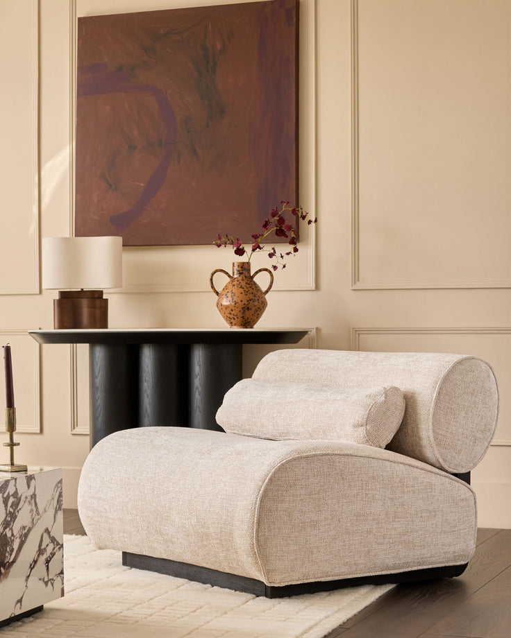 Sofia accent chair in natural fabric with curved rolled arms and black base, styled in modern living room.