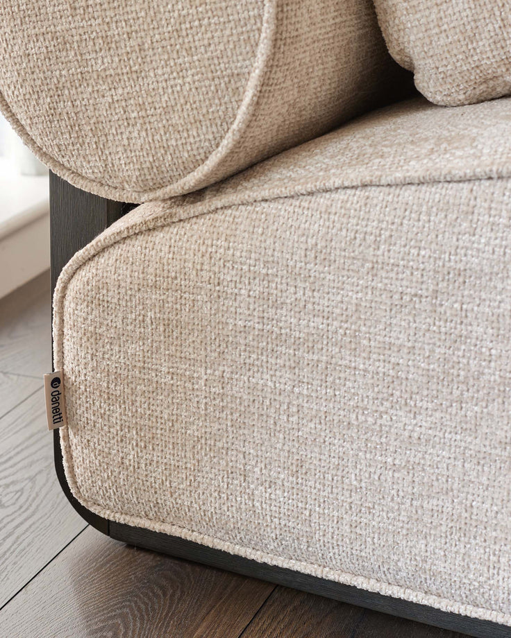 Sofia 2-seater sofa in natural fabric, close-up detail showing woven texture and branded handle tag on wooden base.