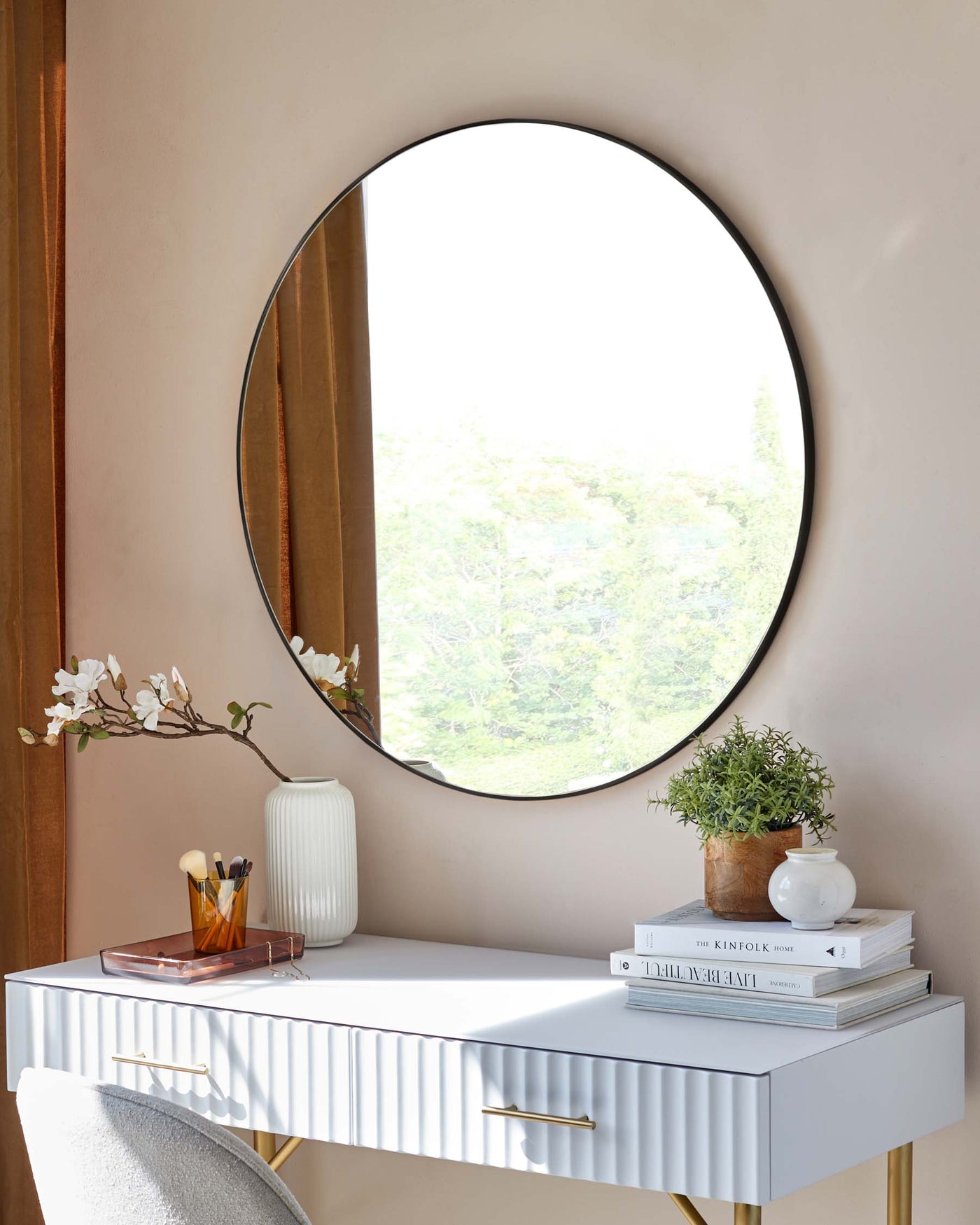 A modern white console table with fluted drawer fronts and brass handles, set against a light earth-toned wall with a large round mirror above it.