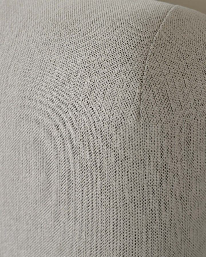 Close-up of a textured, light grey fabric on furniture, possibly a sofa or chair, showing detailed weave and seam.