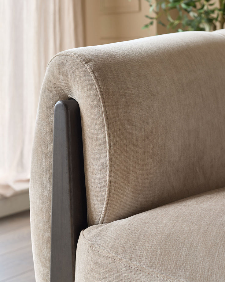 Close-up of champagne fabric upholstery and dark wooden arm detail on Teagan two-seater sofa.