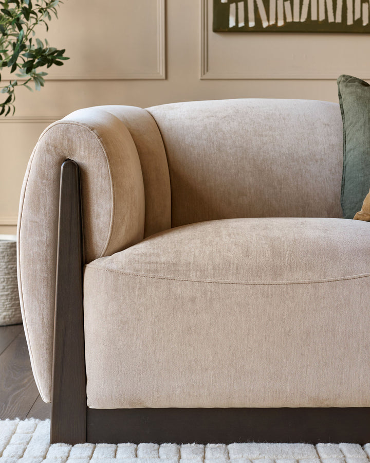 Teagan 2-seater sofa in champagne fabric with curved arms, dark wood legs, and rolled back detail, angled side view.