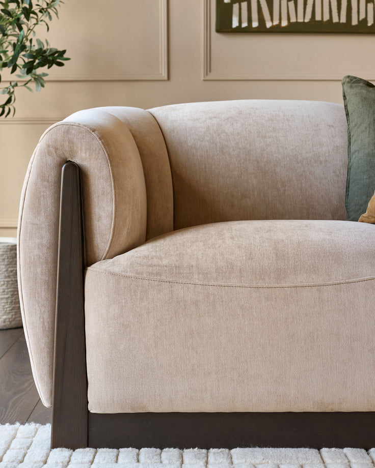 Teagan 2-seater sofa in champagne fabric with curved arms, dark wood legs, and rolled back detail, angled side view.