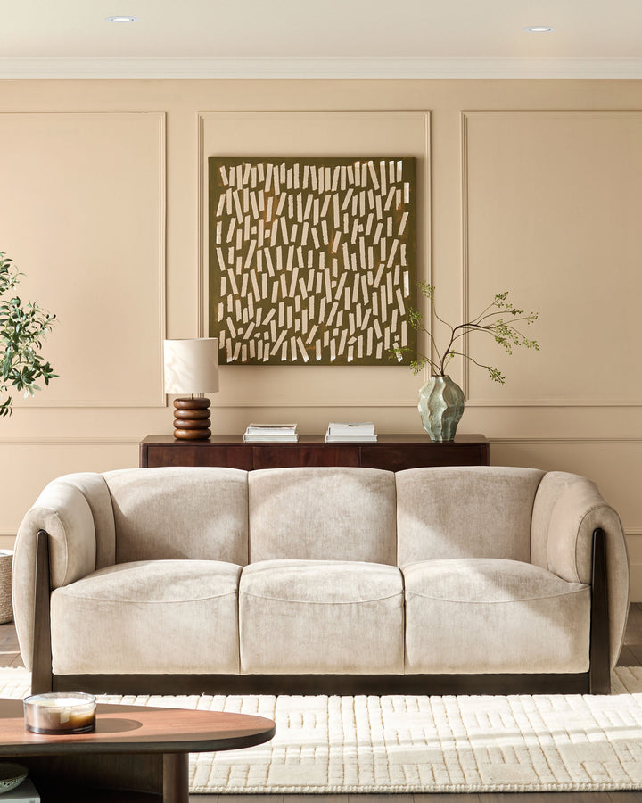 Teagan 3-seater sofa in champagne fabric with curved arms and dark wood base, displayed in a neutral living room setting.