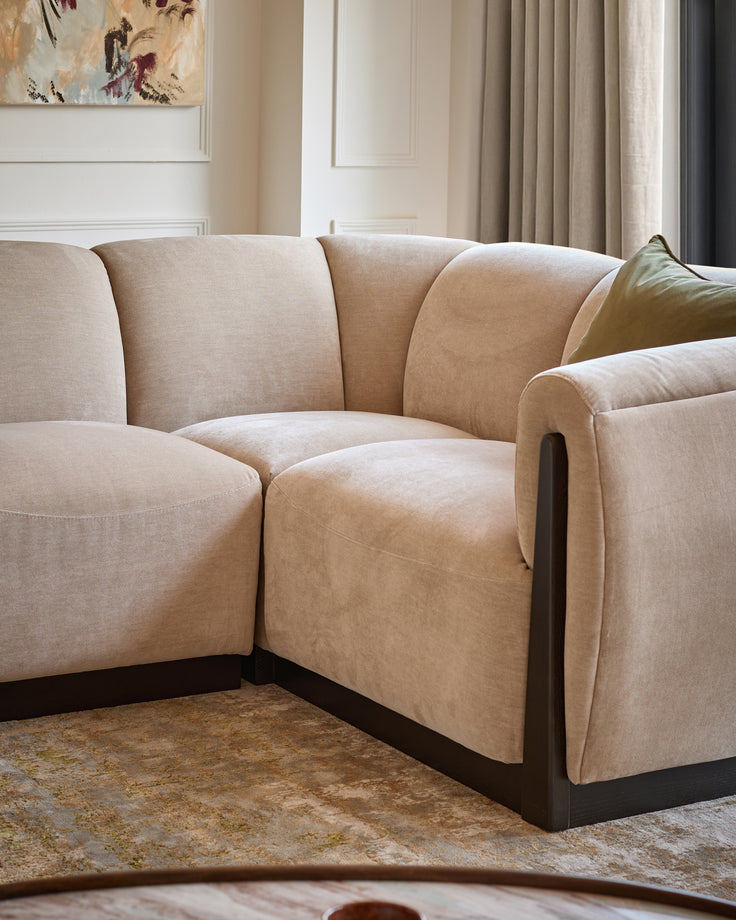 Teagan right-hand small corner sofa in champagne fabric with curved arms and dark wooden base, angled view.