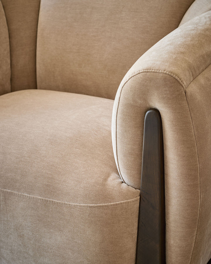 Teagan armchair in champagne fabric, close-up detail of curved arm with dark wood handle and stitched seam.
