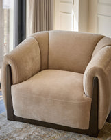 Teagan armchair in champagne fabric with curved arms and dark wood base, positioned in a bright room.