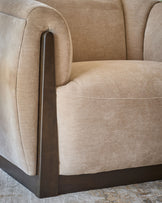 Teagan armchair in champagne fabric with curved back, rounded seat, and dark wood armrest and base detail.
