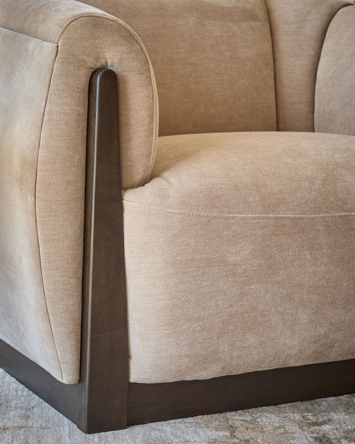 Teagan armchair in champagne fabric with curved back, rounded seat, and dark wood armrest and base detail.