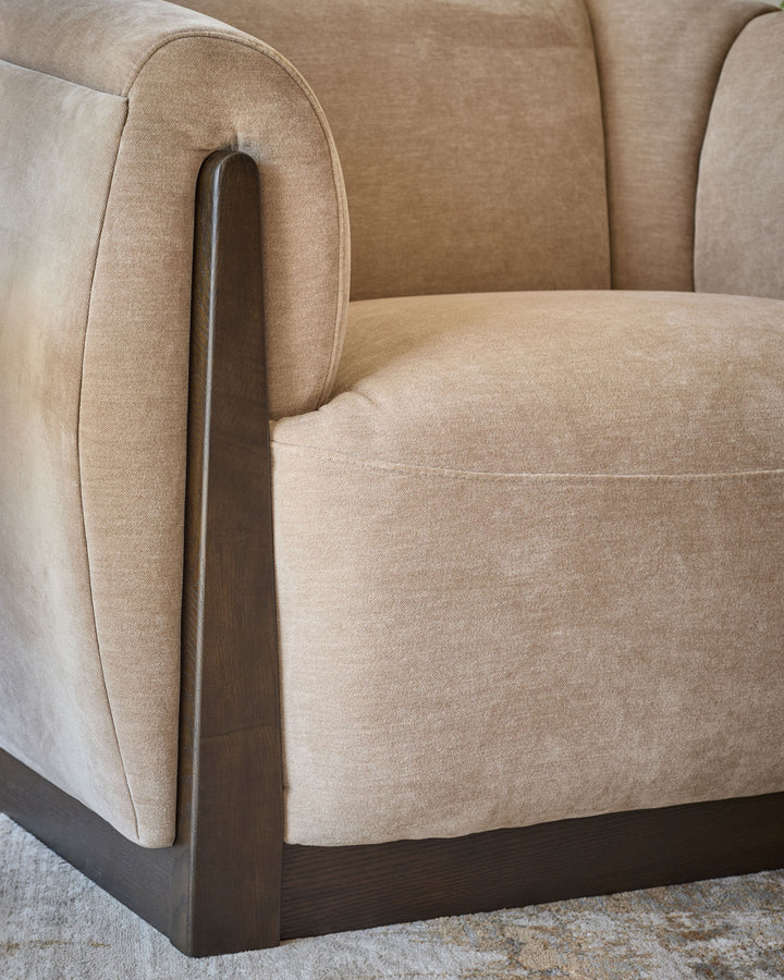 Teagan armchair in champagne fabric with curved back, rounded seat, and dark wood armrest and base detail.