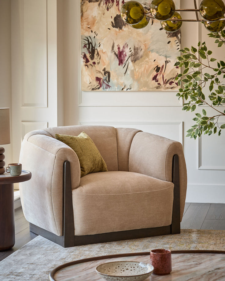 Teagan armchair in champagne fabric with curved arms, dark wood frame, and olive accent pillow in styled living room.