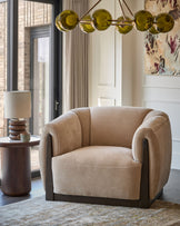 Teagan armchair in champagne fabric with curved arms and dark wood base, positioned in a modern living room setting.