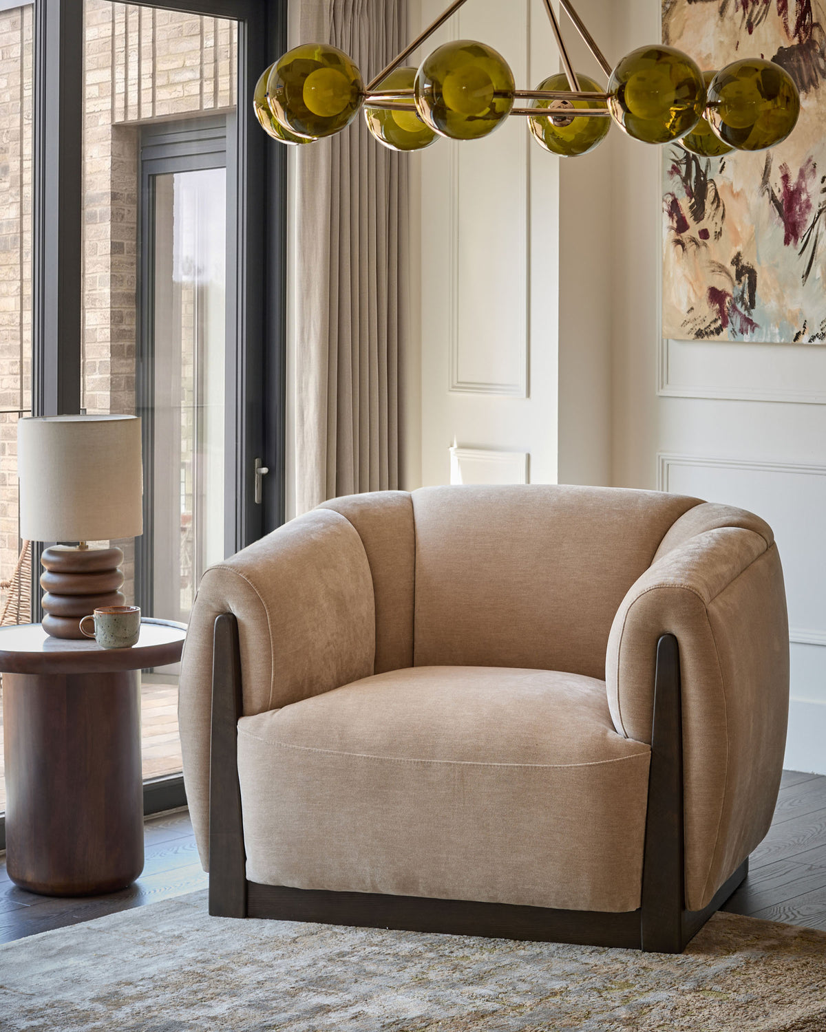 Teagan armchair in champagne fabric with curved arms and dark wood base, positioned in a modern living room setting.