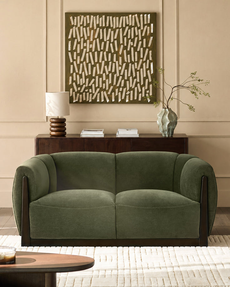 Teagan 2-seater sofa in olive green fabric with dark wood frame and armrests, displayed in a styled living room setting.
