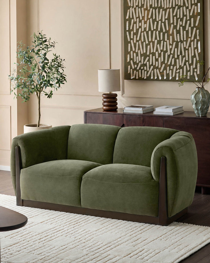 Teagan 2-seater sofa in olive green fabric with curved arms and dark wood base, displayed in a styled living room setting.