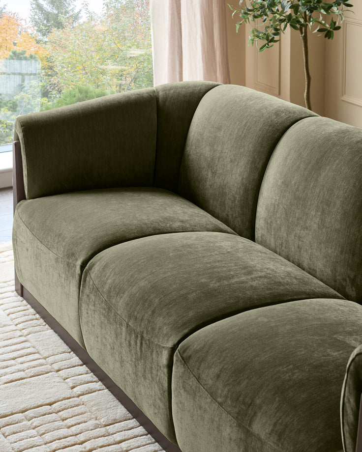Teagan 3-seater sofa in olive green fabric, showcasing curved design and plush cushioning in a bright, modern living room setting.