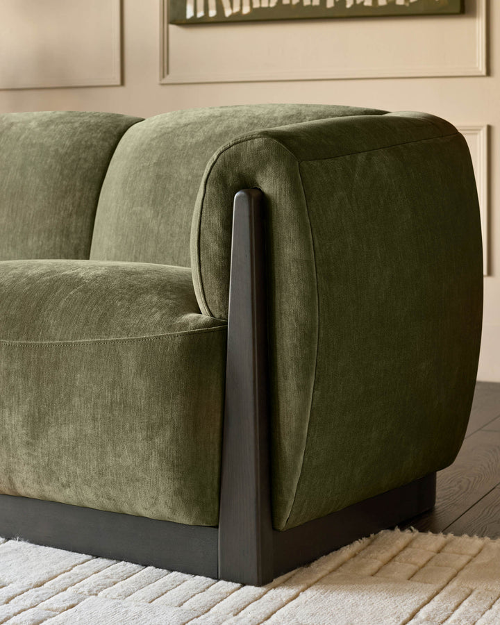 Teagan 3-seater sofa in olive green fabric with dark wooden armrest detail, shown from side angle on light wooden floor.
