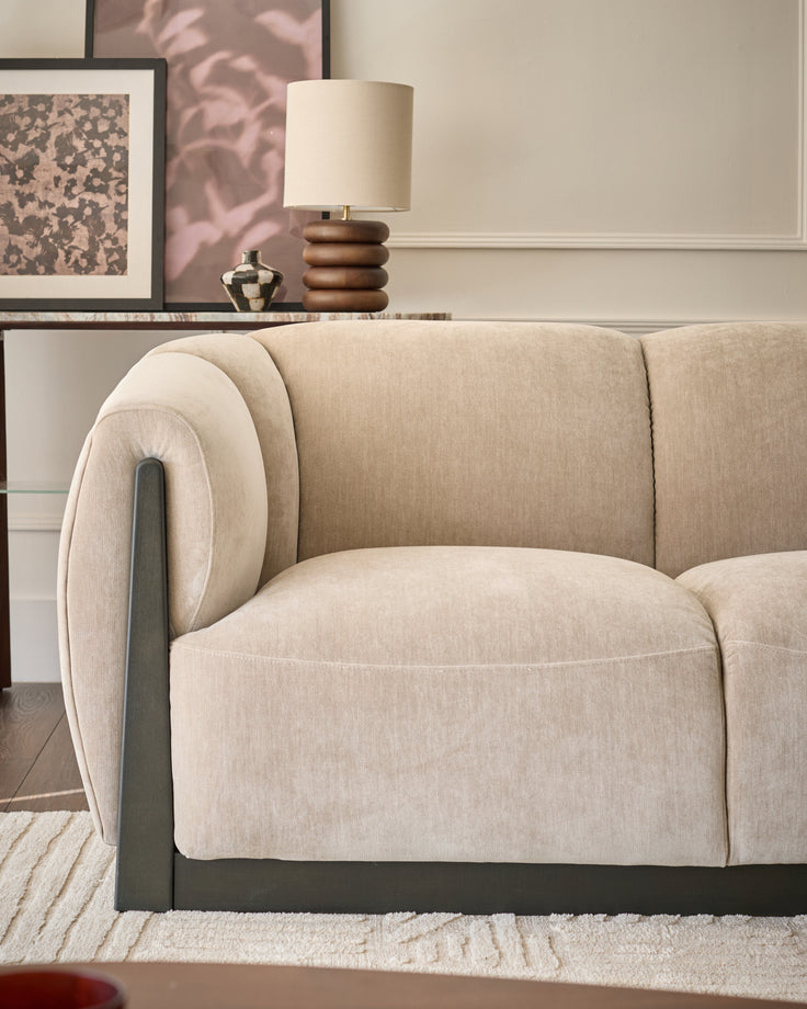 Teagan 2-seater sofa in champagne fabric with curved arms and dark wooden legs, angled side view.
