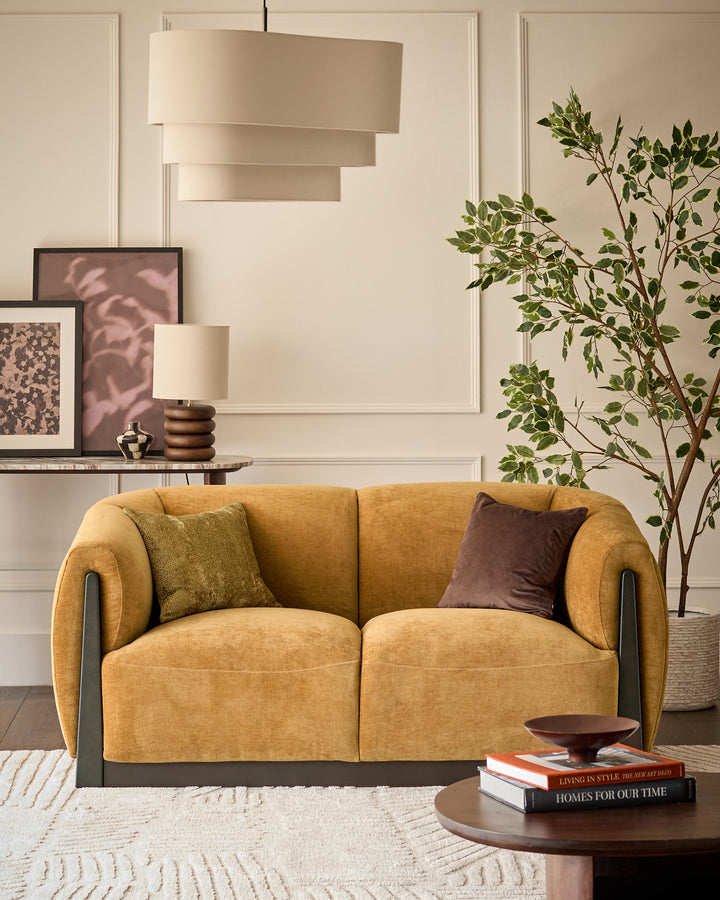 Teagan 2-seater sofa in ochre fabric with curved arms and dark wood accents, styled in a modern living room.